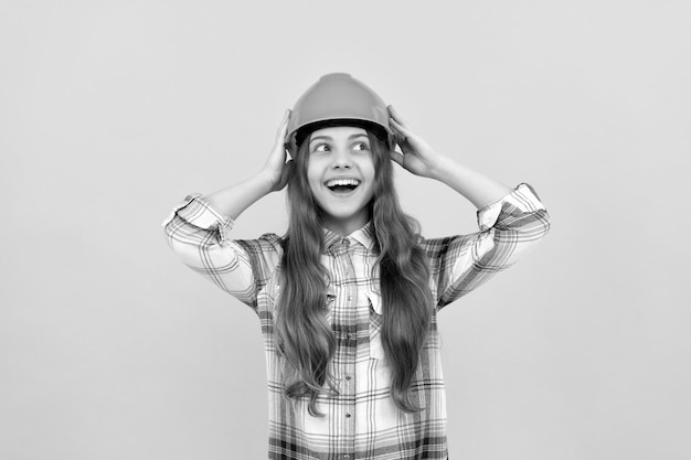 Happy teen girl in helmet and checkered shirt carpenter