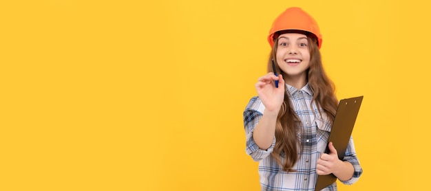 Happy teen girl in helmet and checkered shirt making notes on clipboard childhood Child in hard hat horizontal poster design Banner header copy space