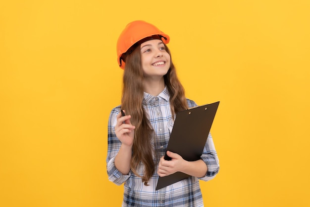 Happy teen girl in helmet and checkered shirt making notes on clipboard inspector