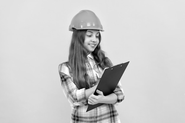 Happy teen girl in helmet and checkered shirt making notes on clipboard make notes