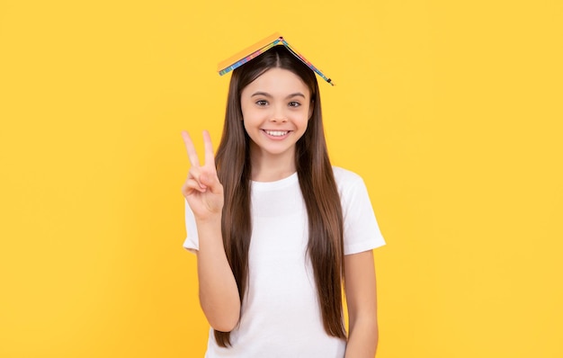 Happy teen girl hold book showing peace on yellow background school