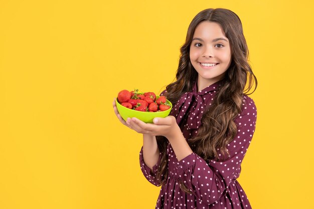 Happy teen girl hold strawberry bowl on yellow background copy space