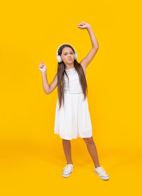 Happy teen girl listen music in headphones and having fun on yellow background