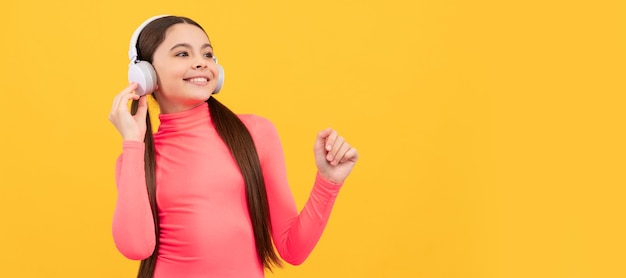 Happy teen girl listen music in headphones on yellow background Child portrait with headphones horizontal poster Girl listening to music banner with copy space