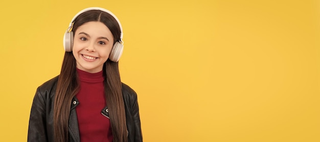 Happy teen girl listen music in headphones on yellow background with copy space Child portrait with headphones horizontal poster Girl listening to music banner with copy space