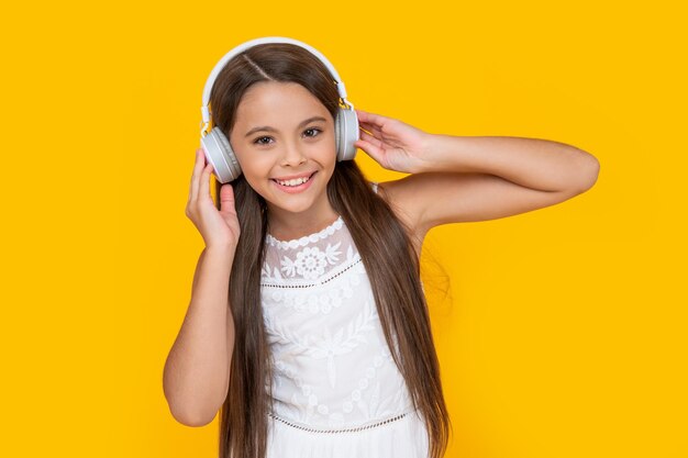 Happy teen girl listening music in headphones on yellow background