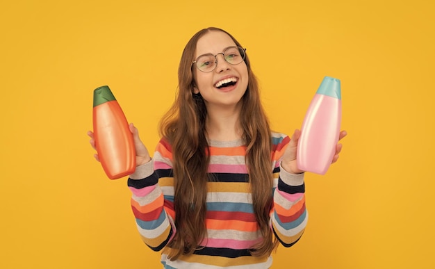 Счастливая девушка-подросток с длинными волосами в очках выбирает между шампунем и советом по бутылке лосьона для тела
