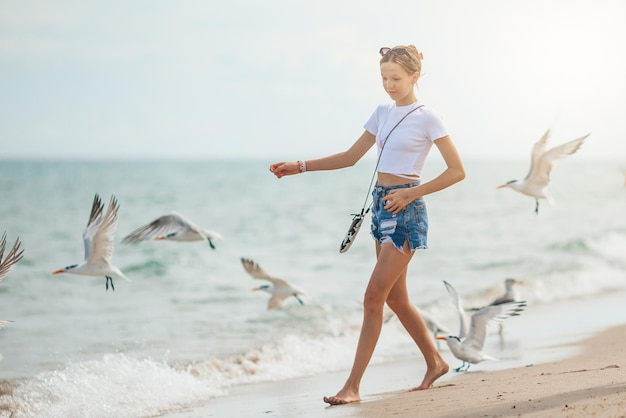 Ragazza teenager felice che gioca con gli uccelli del gabbiano che corrono e si divertono sulla spiaggia in un caldo giorno d'estate vacanze estive in florida