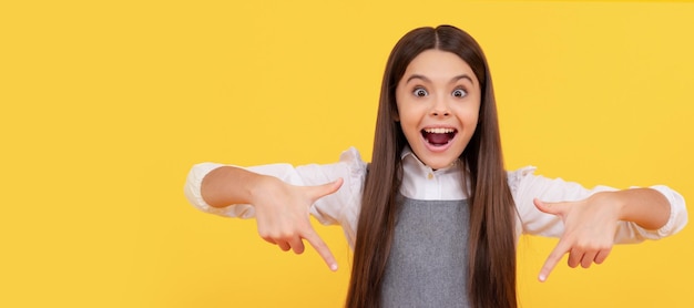 Felice ragazza adolescente punta il dito sul foglio di carta rosa bianco copia spazio promozione bambino faccia orizzontale