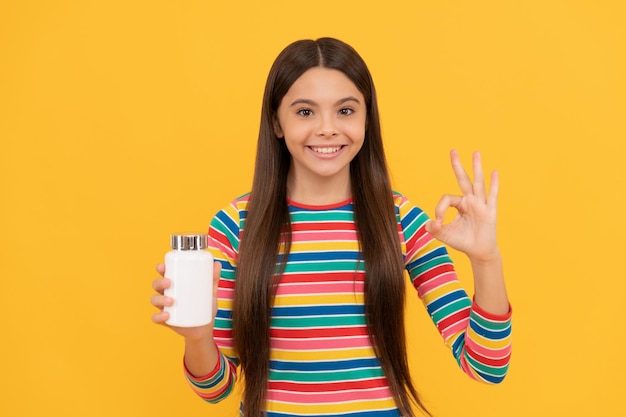 Happy teen girl presenting natural food additives or vitamin\
pills in jar ok