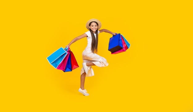 Happy teen girl running with shopping bags on yellow background full length