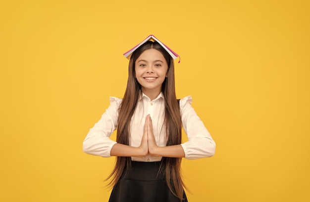 Happy teen girl in school uniform with book on head meditating with hand gesture keep calm