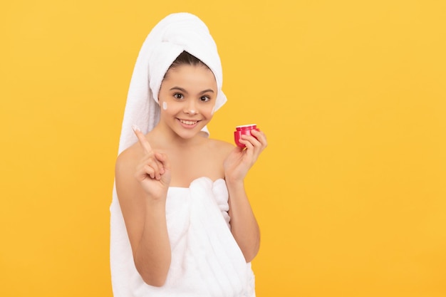 Happy teen girl in shower towel applying facial cream copy space