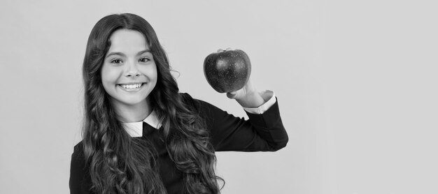 Happy teen girl showing red vitamin apple for lunch on yellow background vitamin Child girl portrait with apple horizontal poster Banner header with copy space