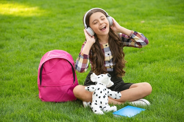 Felice ragazza teenager che canta una canzone sull'erba dopo la musica della scuola torna a scuola allievo a scuola