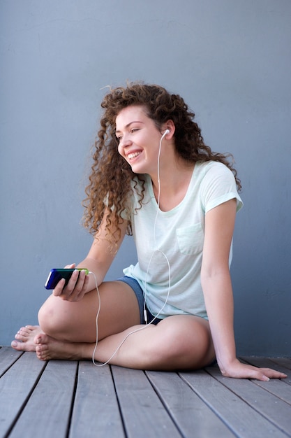 Happy teen girl sitting on floor listening to music