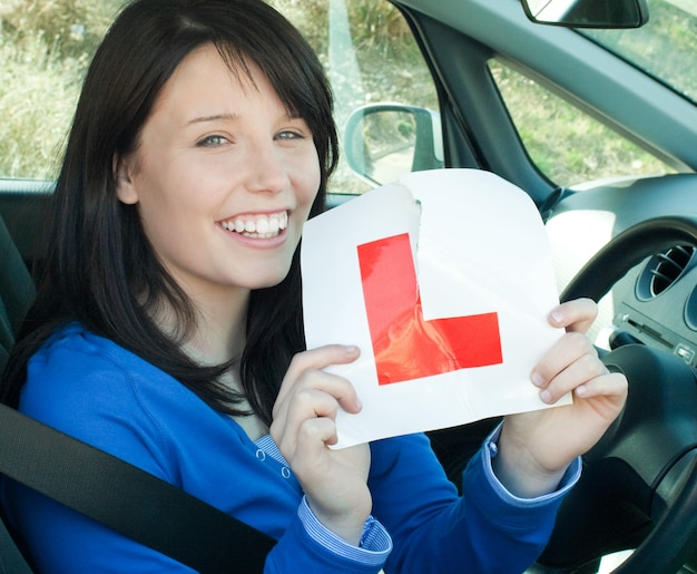 Foto ragazza teenager felice che si siede nella sua automobile che strappa un l-segno