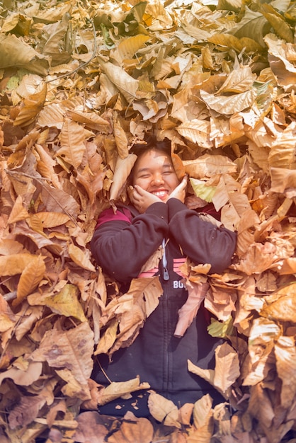 Happy teen girl smiling in a black dress lay down in the autumn of dry leaf.