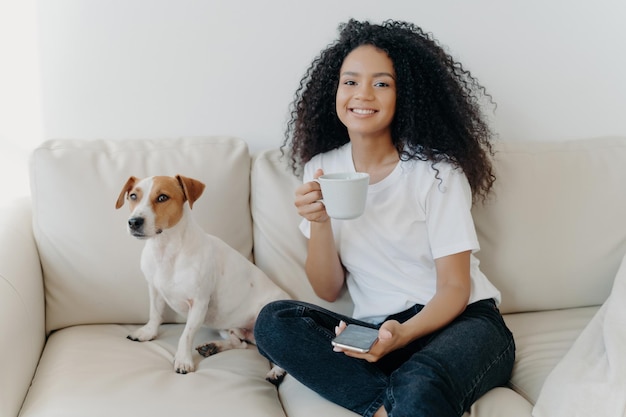 Happy teen girl texts surfs social media connected online cuddles dog sips tea chilling at home