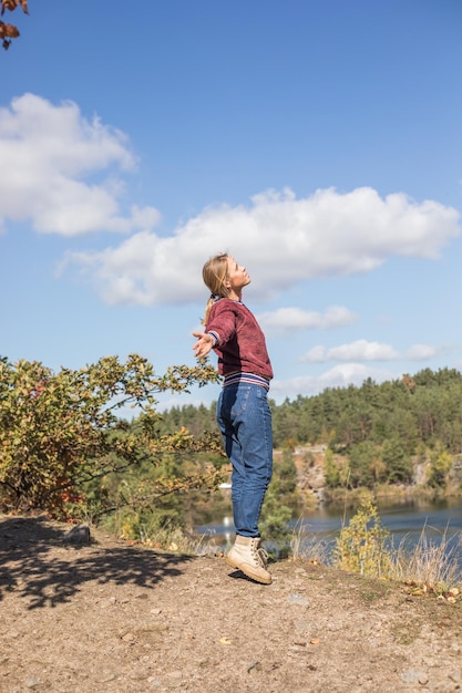 Счастливая девочка-подросток на вершине горы, чувствует себя свободной и смотрит на голубое озеро