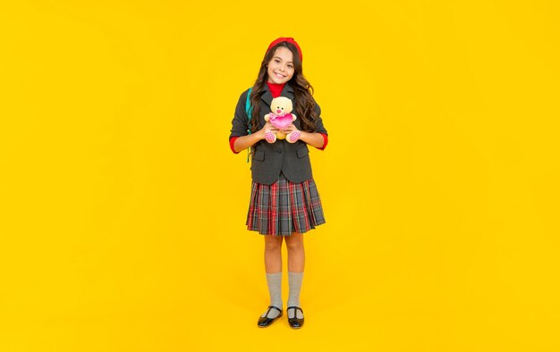 Happy teen girl in uniform with school bag holding toy on yellow background, education.