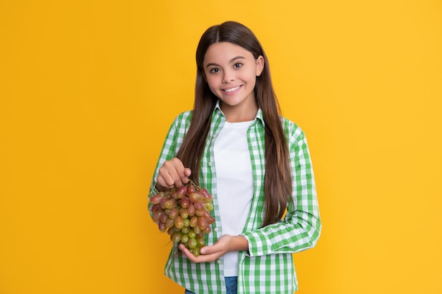 Happy teen girl with fresh grapes bunch on yellow background