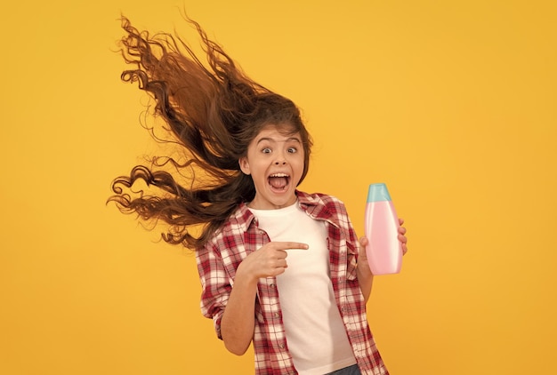 Happy teen girl with long curly hair hold shampoo bottle keratin