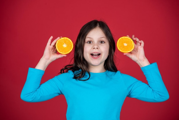 Happy teen kid holding orange fruit on purple background