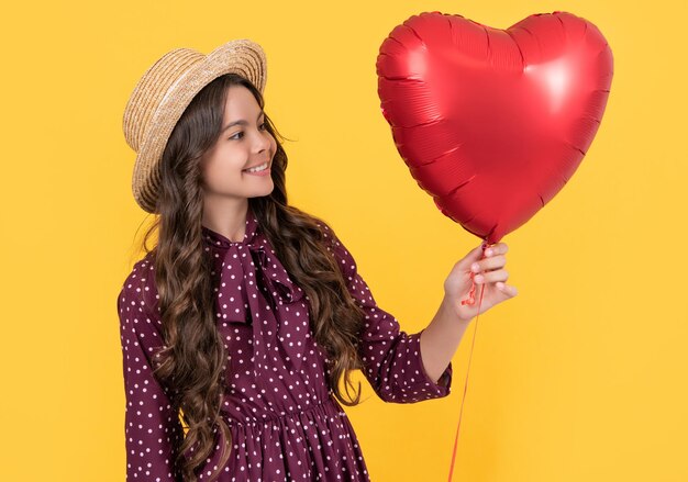 Happy teen kid with red heart balloon on yellow background