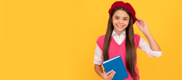 Happy teen school girl in french beret hold copybook on yellow background education Banner of school