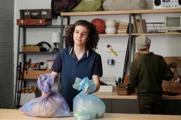 Happy teenage boy with two large cellophane sacks full of waste looking at you