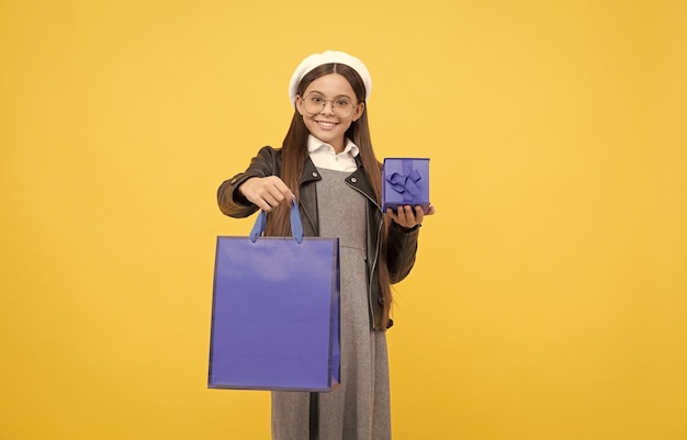 Happy teenage girl back to school holding gift box and paperbag yellow background shopping bag