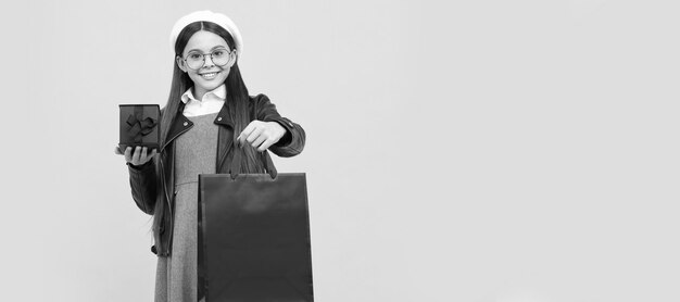 Happy teenage girl back to school holding gift box and paperbag yellow background shopping bag