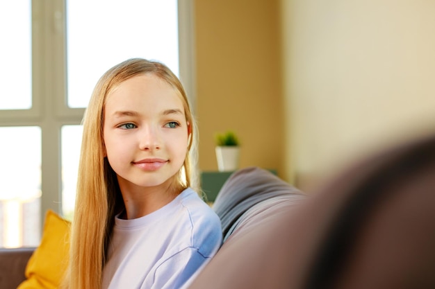 Счастливая девочка-подросток в хлопковой футболке сидит дома на диване