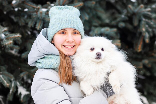 冬の雪の上で彼女の犬と遊ぶのを楽しんで幸せな10代の少女