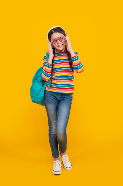 Happy teenage girl listening to music after school yellow background school Music school