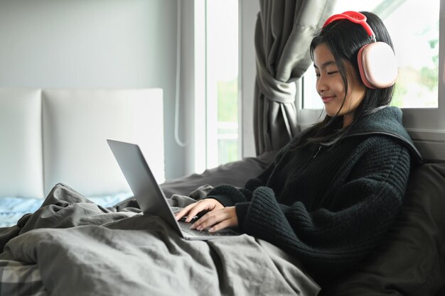 Happy teenage girl looking at laptop studying virtual course learning distance class via laptop on bed at home