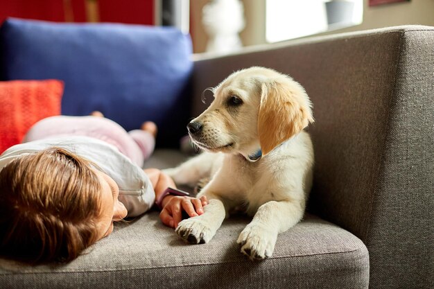 写真 ソファに横たわり、子犬のゴールデンレトリバーを抱きしめる幸せな10代の少女