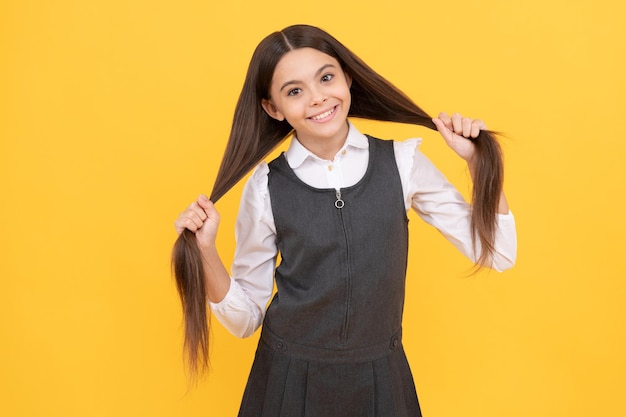 Happy teenage girl in school uniform smile holding long hairstyle yellow background, hair.