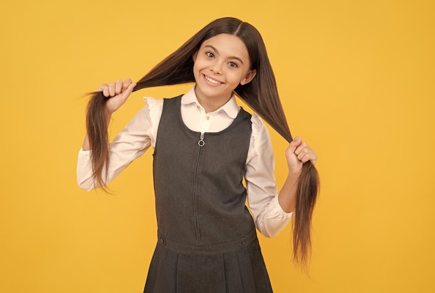 Happy teenage girl in school uniform smile holding long hairstyle yellow background hair