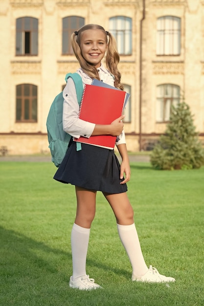 Happy teenage girl in school uniform standing in front of school back to school september 1 education and schooling