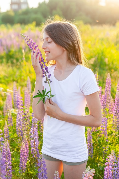 幸せな10代の少女が屋外で笑っています。咲く野生の花の緑の背景と夏のフィールドで休んでいる美しい若い10代の女性