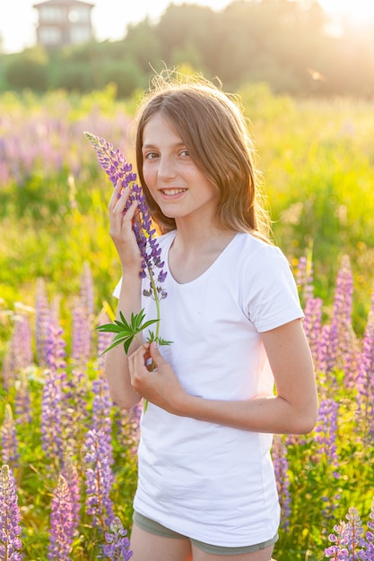 幸せな10代の少女が屋外で笑っています。咲く野生の花の緑の背景と夏のフィールドで休んでいる美しい若い10代の女性