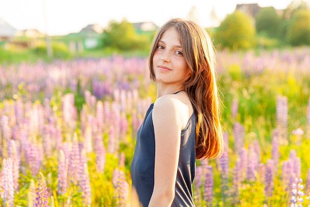 Happy teenage girl smiling outdoor. Beautiful young teen woman resting on summer field with blooming wild flowers green background