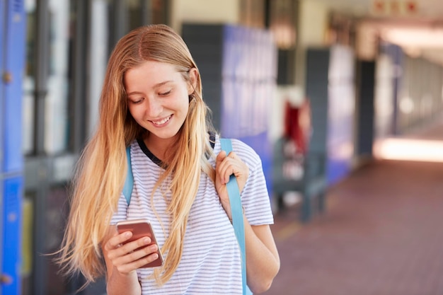 Happy teenage girl using smartphone in school corridor