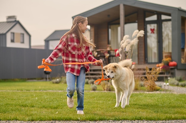 庭の芝生の上をふわふわの柴犬と一緒に歩いている幸せな 10 代の少女