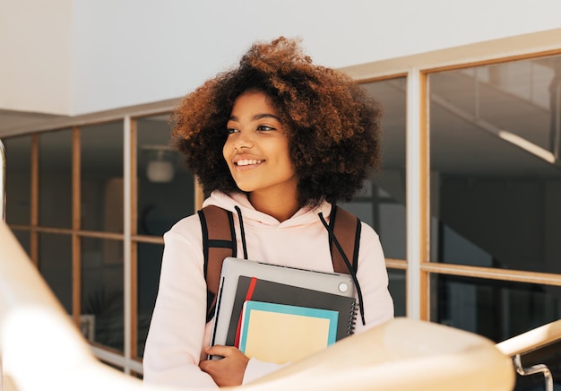 Photo happy teenage girl with laptop and books standing against glass wall