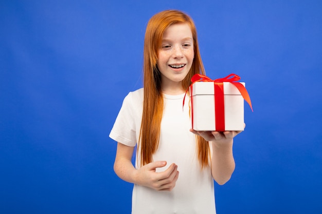 Happy teenage girl with red hair received a birthday present on a blue studio background