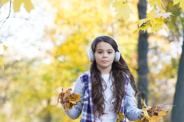 Happy teenage kid listen music wearing headphones in autumn forest with beautiful seasonal nature or having online lesson music