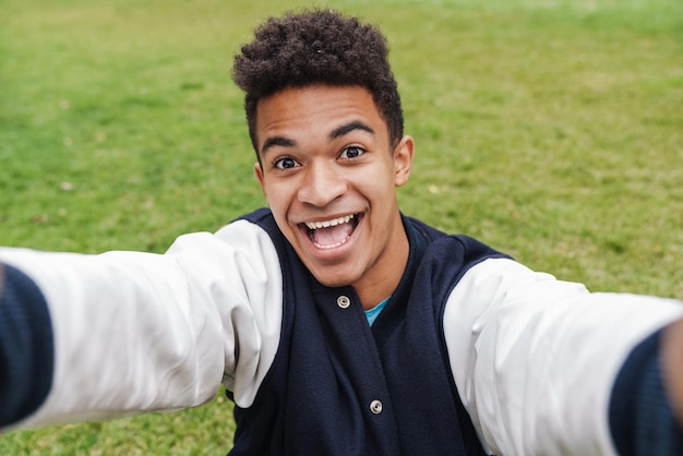 Happy teenager boy taking a selfie while standing on a lawn